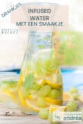 Een karaf gevuld met water, druiven, citroen en ijs op een houten tafel. Bovenin een tekst: drankje, infused water met een smaakje, makkelijk recept