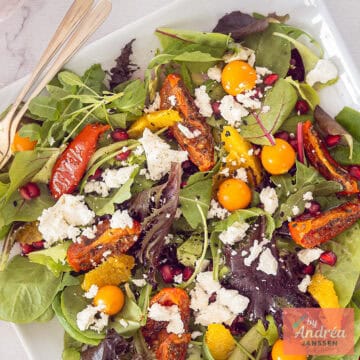 Een vierkante foto met een salade met feta, goudbessen, zongedroogde tomaten en sinaasappel