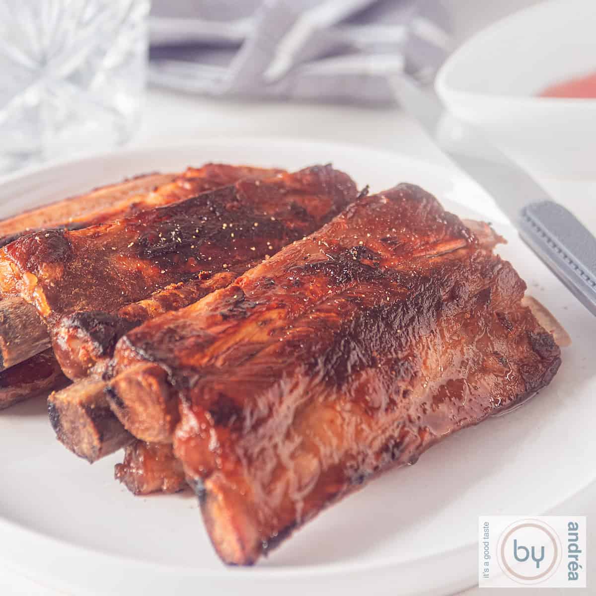 Een vierkante foto met een bord met een stapel honing ketjap whisky ribjes.