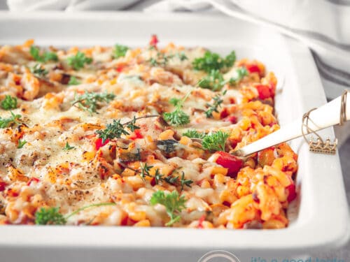 Een macaroni ovenschotel in een witte schaal. Op de achtergrond een grijs wit gestreepte handdoek