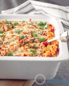 Een witte ovenschaal gevuld met macaroni, kaas, mascarpone en tomatensaus en lekkere groenten. Een wit grijze handdoek licht op de achtergrond