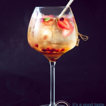A black background with a glass filled with sangria with fresh summer fruit and licor 43. A golden spoon stand inside the glass