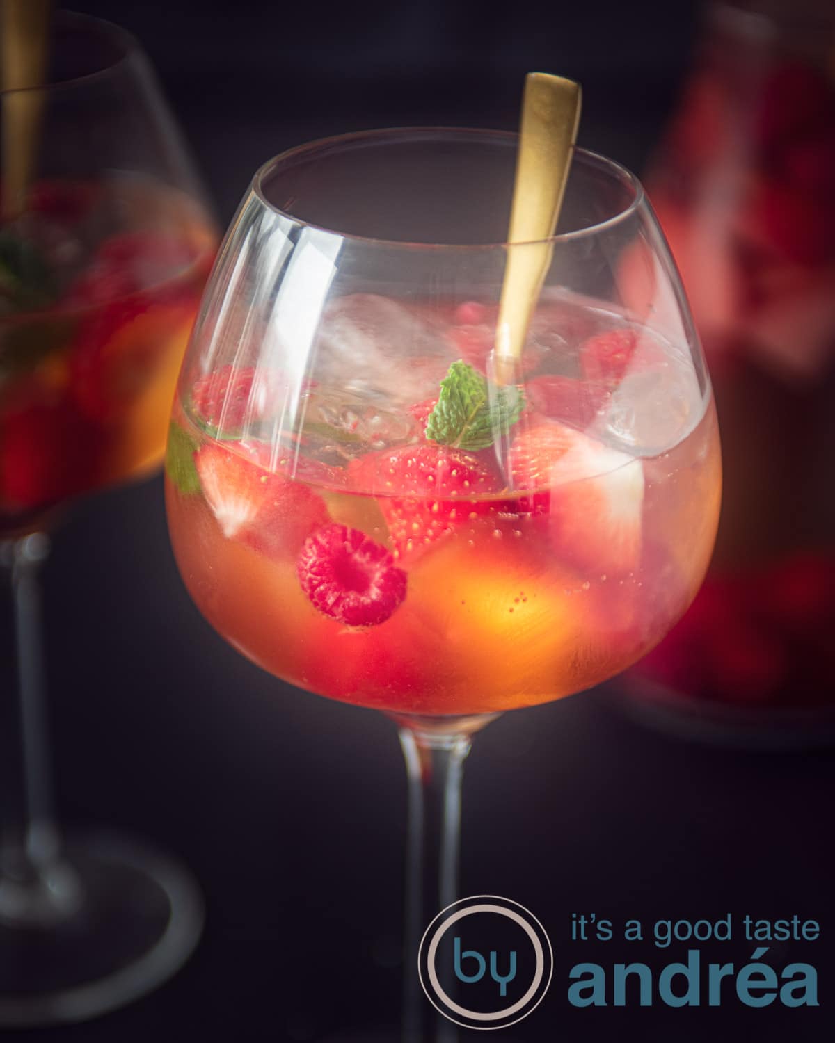 A glass filled with white sangria 43 on a black background. A jar and another glass are in the background