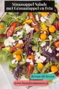 Een foto van een gemengde salade met goudbes, sesam, sinaasappel tomaatje en granaatappel met feta. Een tekst bovenin: Sinaasappel Salade met Granaatappel en Feta