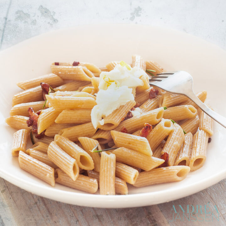 een wit bord met Spelt penne met rozemarijn, spekjes en citroen en getopt met mozzarella