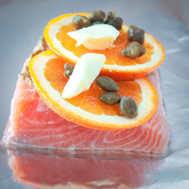 aluminiumfolie daarop zalm met een schijfje sinaasappel, boter en kappertjes