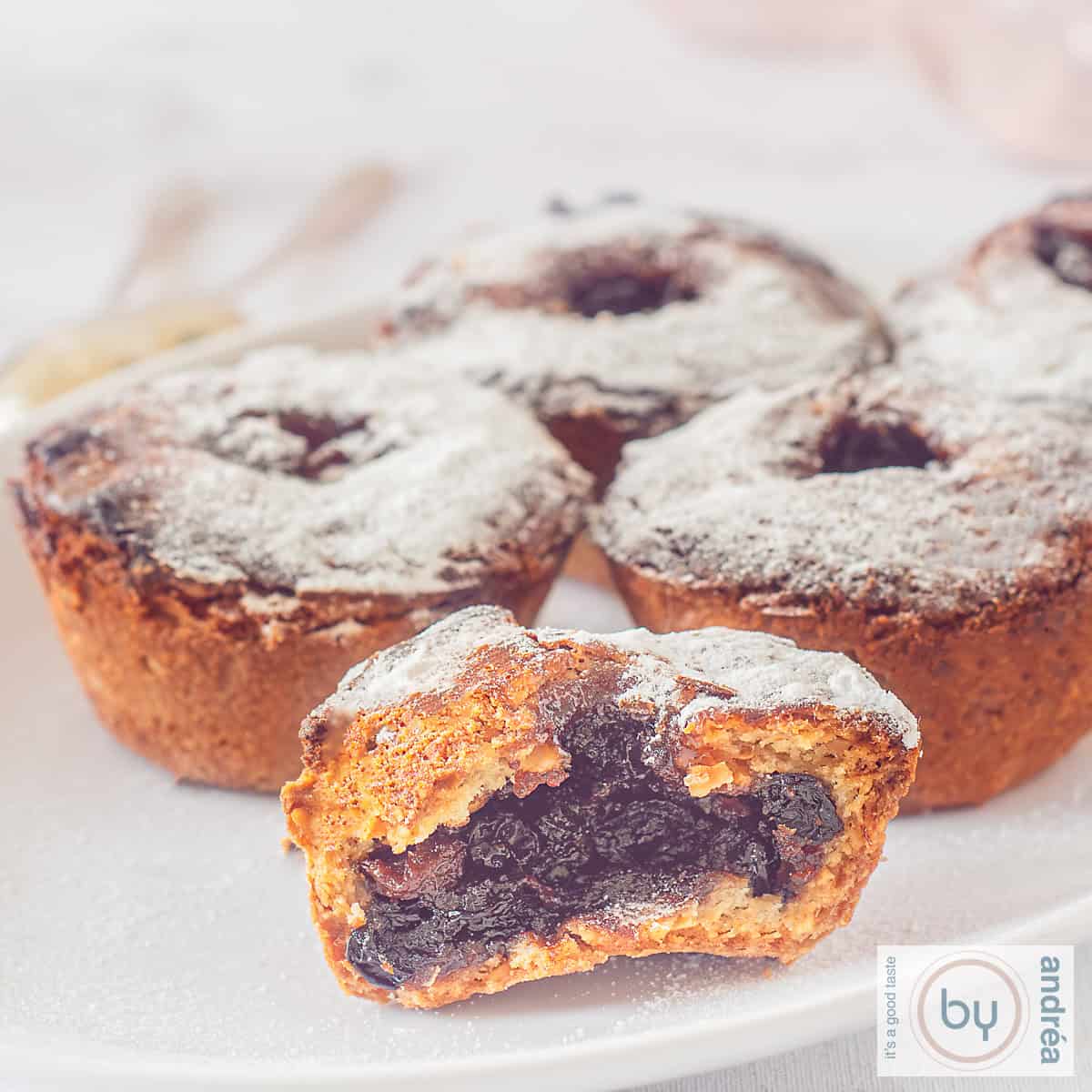 Een vierkante afbeelding met fruit-mince pies op een wit bord. Eén is doormidden en je ziet de fruit-mince vulling.