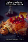 Hand dipt een nachochip in rode tacosaus die in een uitgeholde spinnenkom van hartig deeg zit, met een zwarte spin op de achtergrond tegen een donkere ondergrond