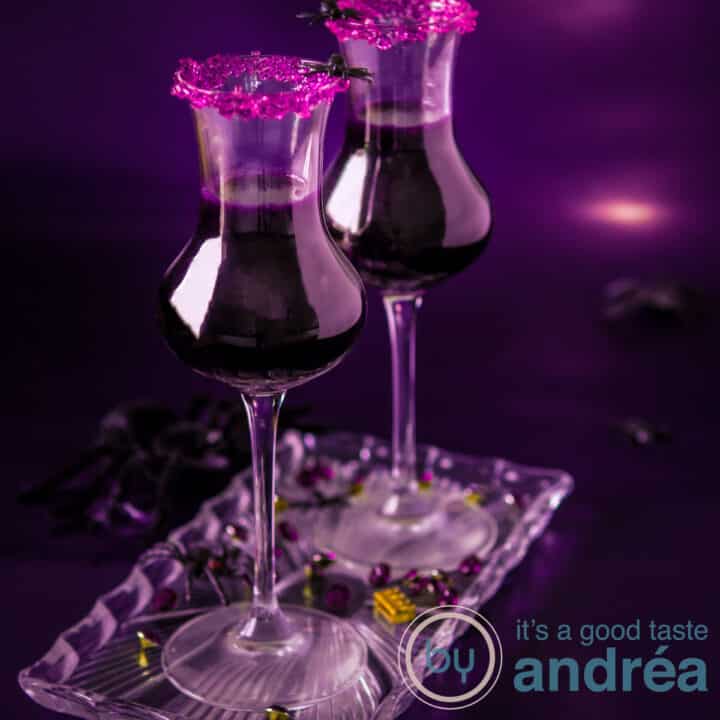 Twee cocktailglazen gevuld met een paarse cocoktail en een paars suikerrandje op een paarse ondergrond.