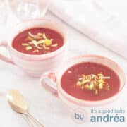 Een vierkante foto met twee roze kopjes gevuld met tomaten prei soep. Een witte ondergrond