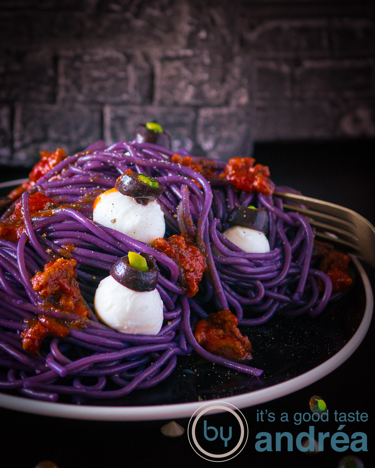 Een zwart bord met paarse spaghetti, bloederige bolognese saus en bolletjes Mozzarella met olijven die eruit zien als ogen.