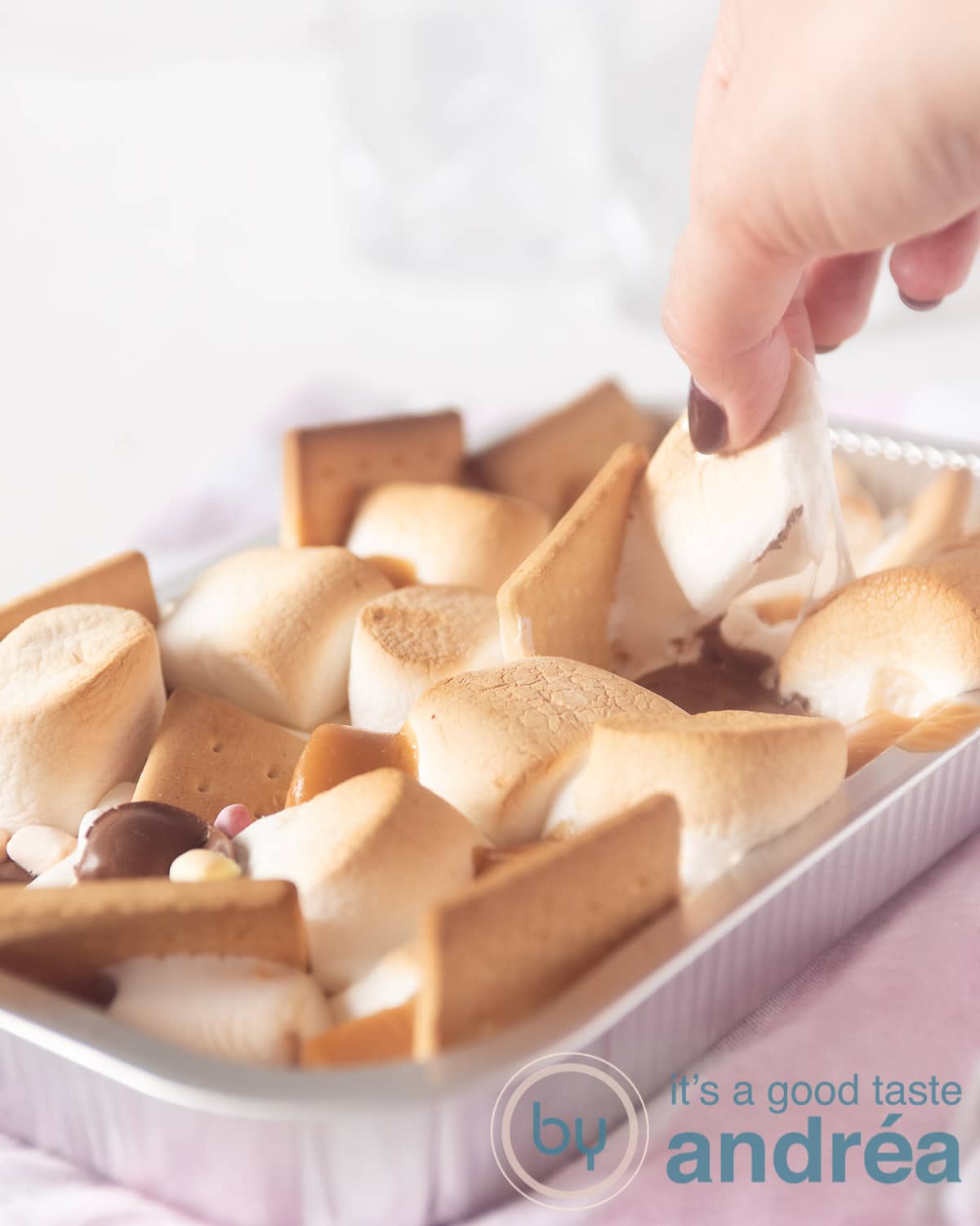 een hand pakt een s'more uit het aluminium bakje