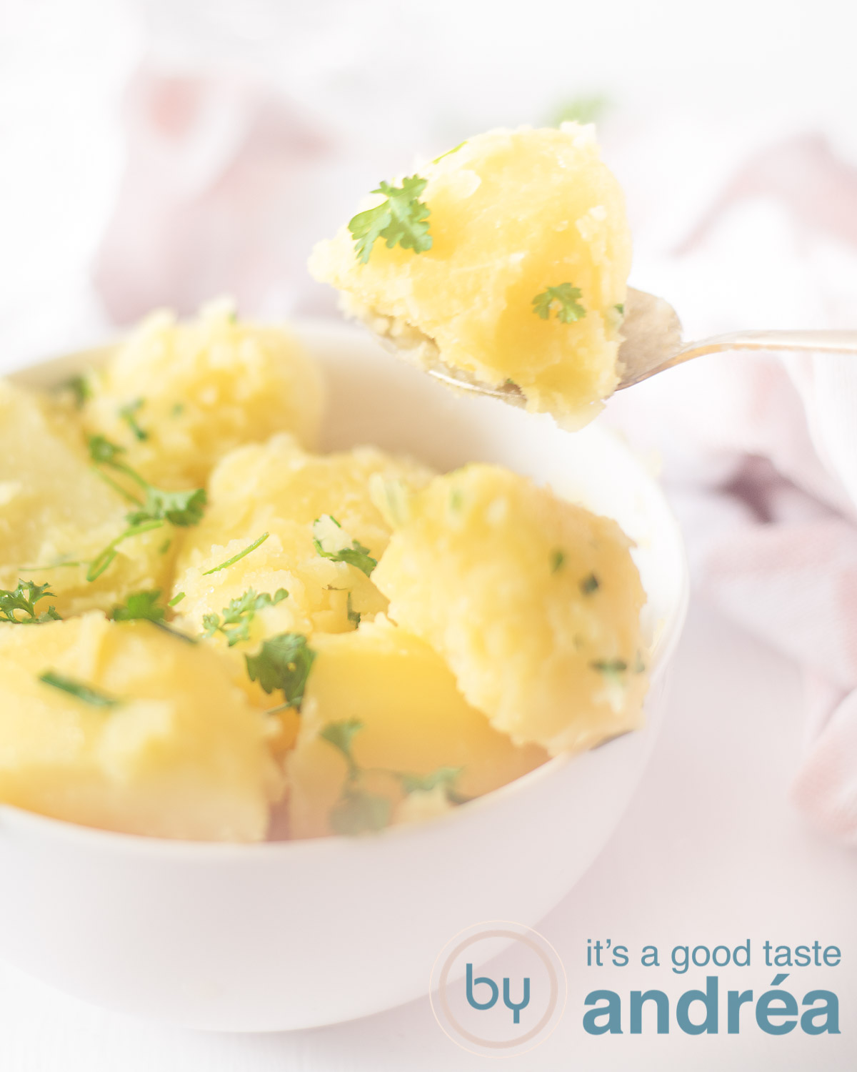 Aardappels met bieslook peterselie boter in een witte schaal een lepel neemt een aardappel uit de schaal. In de achtergrond een roze witte theedoek.
