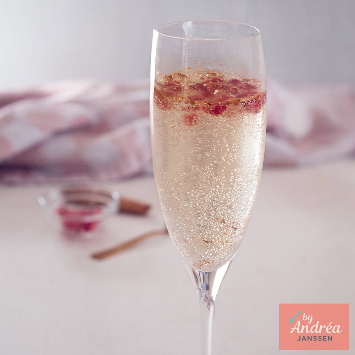 Een vierkante foto van een deel van een champagneglas gevuld met prosecco granaatappelpitjes en kaneel