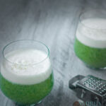 twee glazen gevuld met broccoli soep met een kruidige slagroom topping