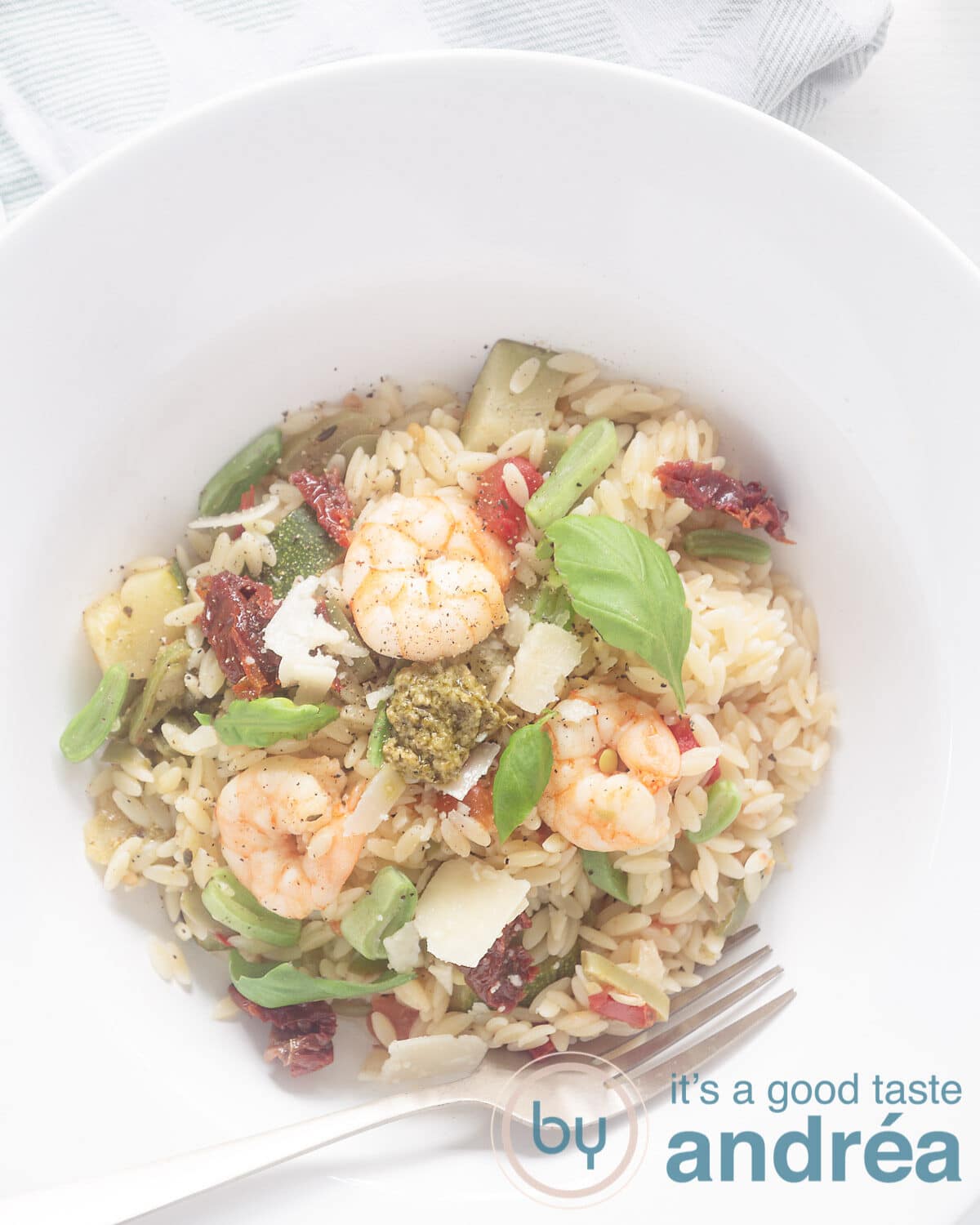 Een foto van bovenaf van een wit diep bord gevuld met Parmezaanse orzo met pesto, snijbonen, courgette en garnalen