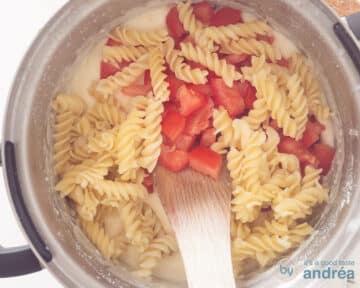Pasta en tomaten worden met de saus geemengd in een pan.