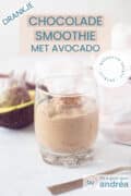 Een glas gevuld met een chocolade smoothie op een witte ondergrond. Een halve avocado en een roze witte theedoek in de achtergrond. Een textoverlay: drankjes, chocolade smoothie met avocado, makkelijk recept, ontbijt