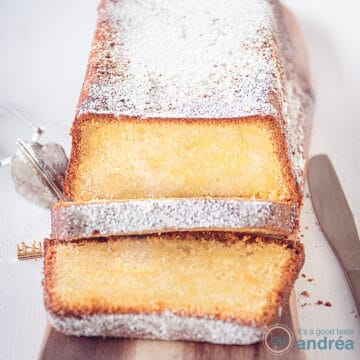 Een vierkante foto met een houten plank met daarop een cake gemaakt met roomkaas en zure room. Twee plakjes erafgesneden. Een witte ondergrond.