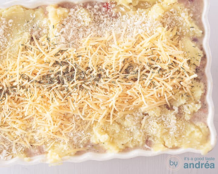 Een breedtefoto met een ovenschaal met aardappelpuree bestrooid met panko, geraspte kaas en tijm