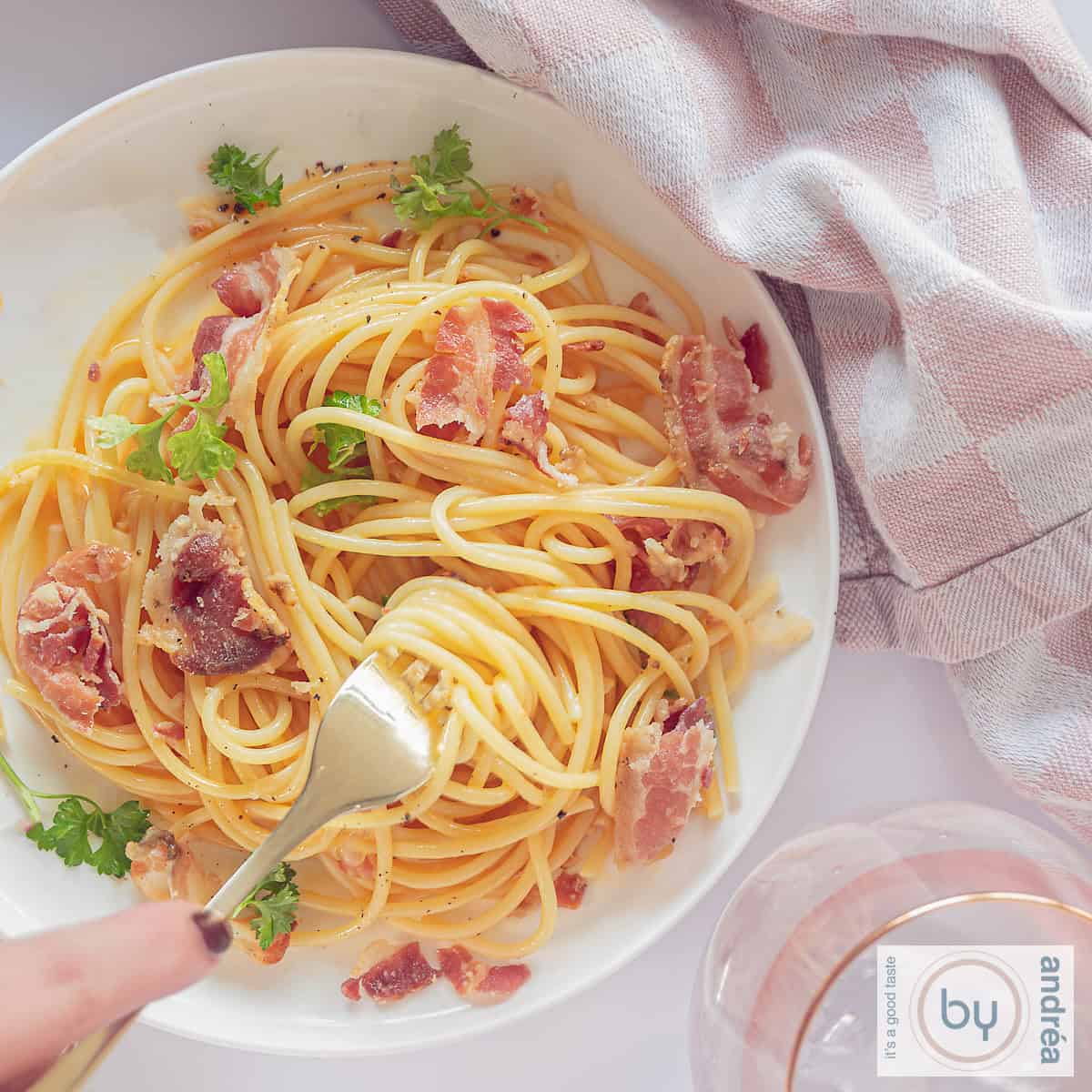 Een vierkante foto van bovenaf genomen vanaf een wit bord zonder pasta carbonara. Een vork prikt in de spaghetti