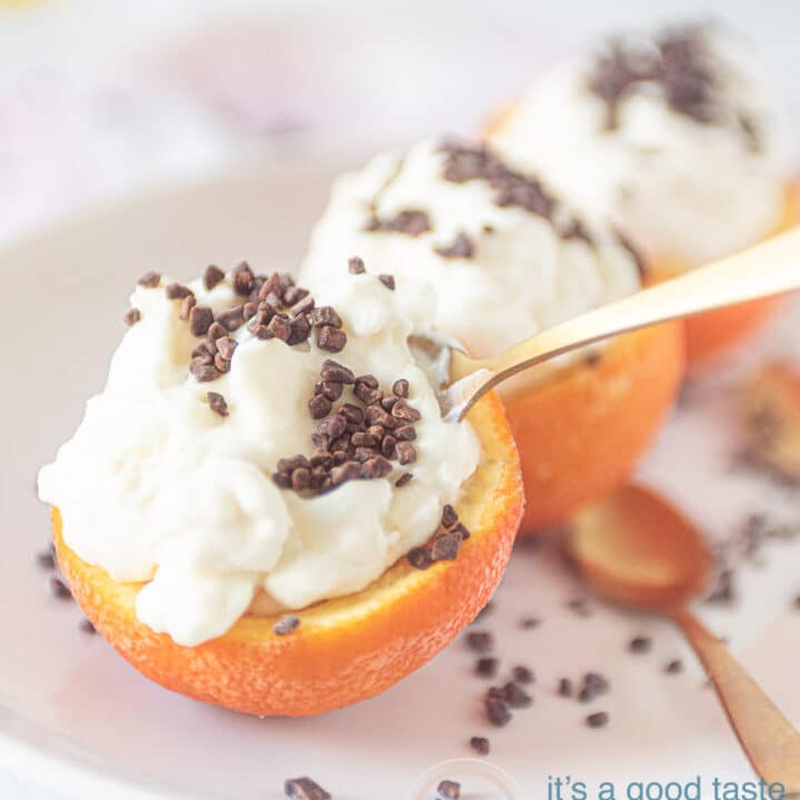 drie halve sinaasappels op een wit bord. Deze zijn gevuld met sinaasappel semifreddo en bestrooid met chocola