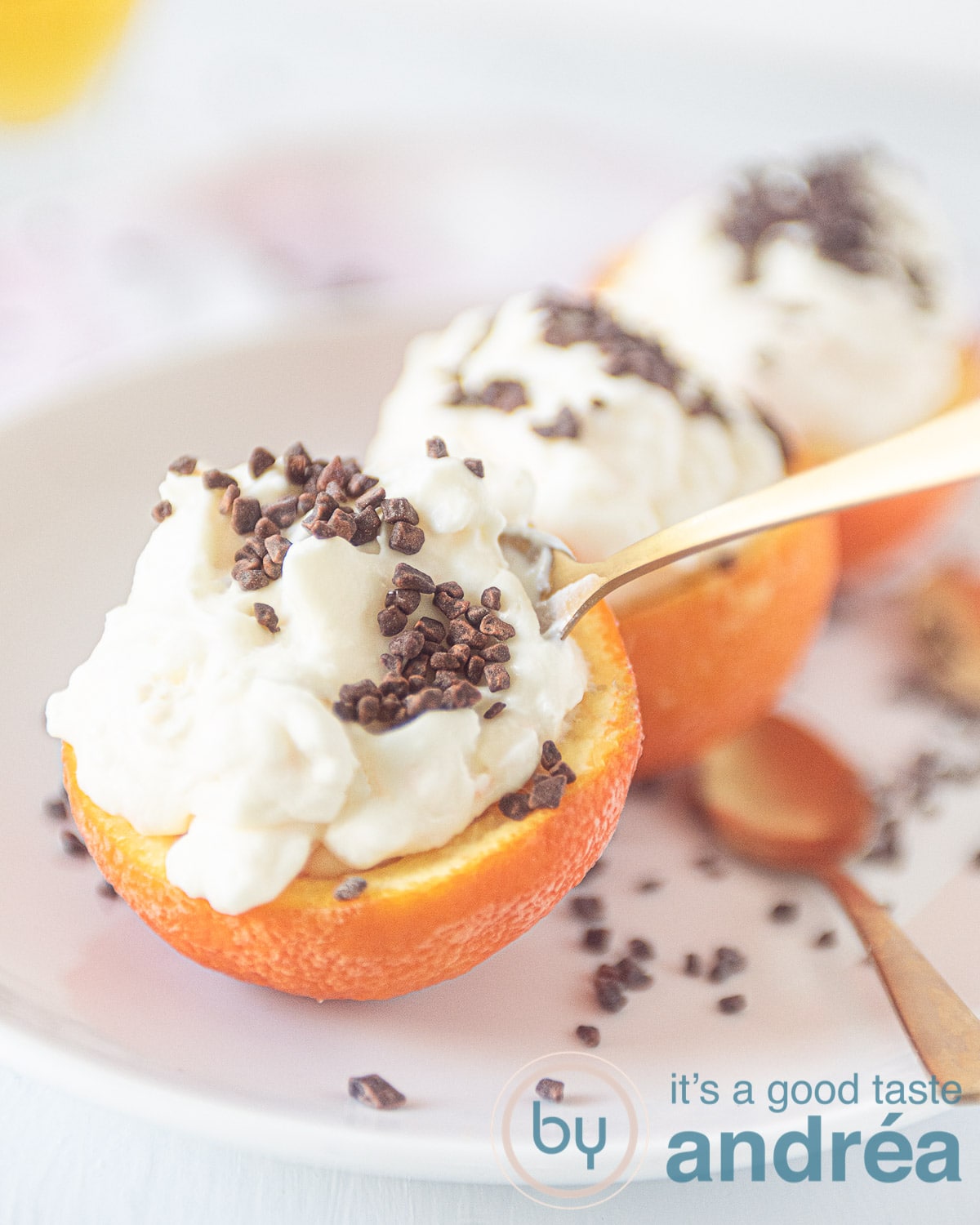 drie halve sinaasappels op een wit bord. Deze zijn gevuld met sinaasappel semifreddo en bestrooid met chocola