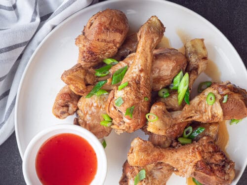 een bord met kip drumsticks in soja saus en een kommetje met chilisaus