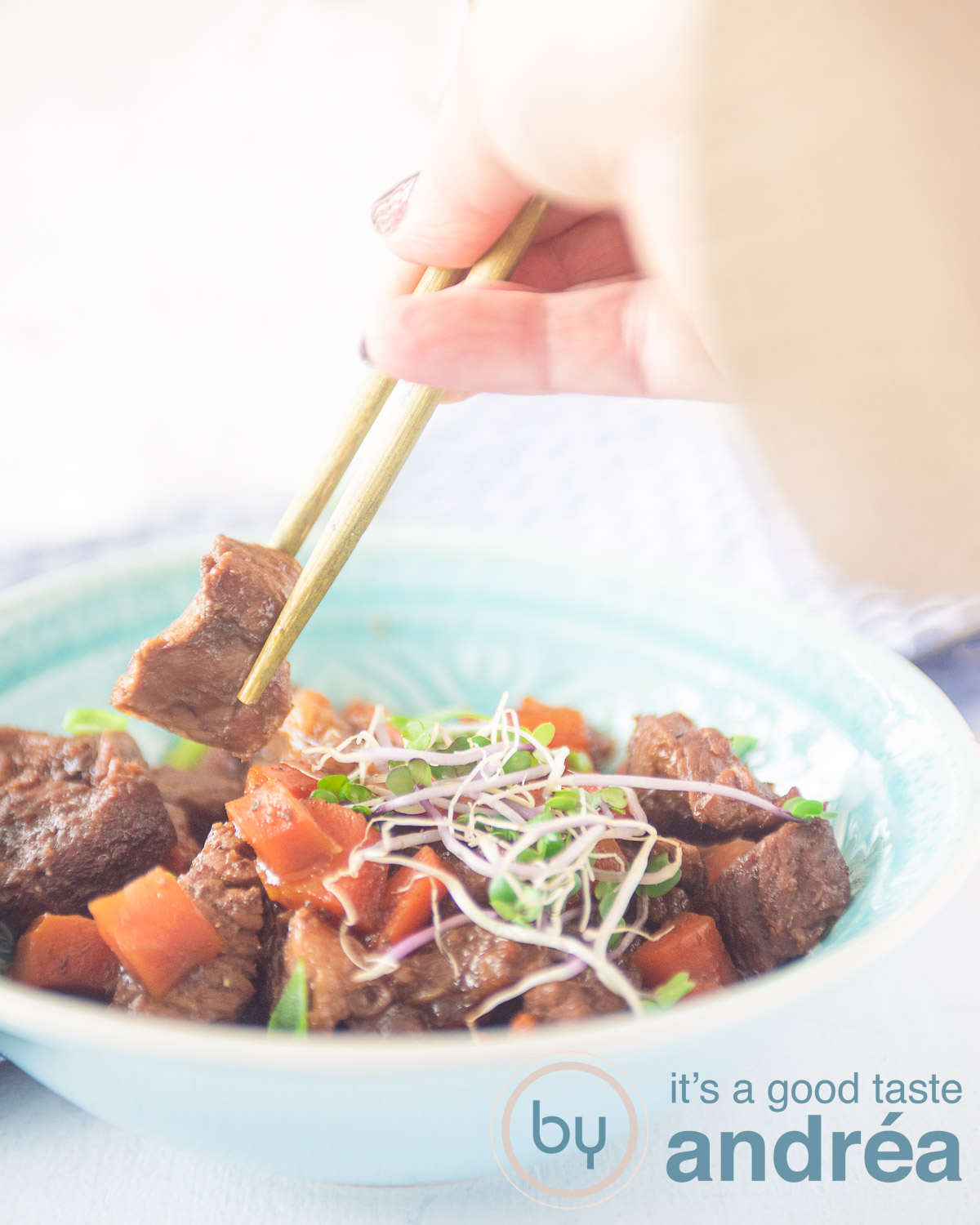 Slow cooker Mongolian beef with carrot in a blue dish. Two golden chopsticks grab a piece of meat.