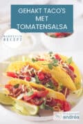 Een wit bord met drie taco's gevuld met gehakt, tomatensaus, kaas en tomaat. Een sausje en crème fraîche in de achtergrond. Een tekst: Gehakt Taco's met Tomatensalsa, makkelijk recept