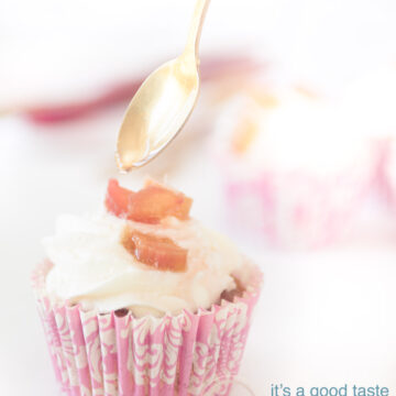 Een roze wite cupcake vorm gevuld met een rabarber muffin met een slagroom topping met rabarber. Een lepel sprenkelt wat siroop op de rabarber