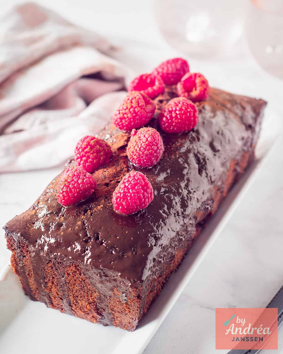 A cake, unsliced, chocolate with raspberries and a drip of chocolate ganache.