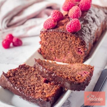 Een vierkante foto met chocoladecake met frambozen waar twee plakjes afgesneden zijn.