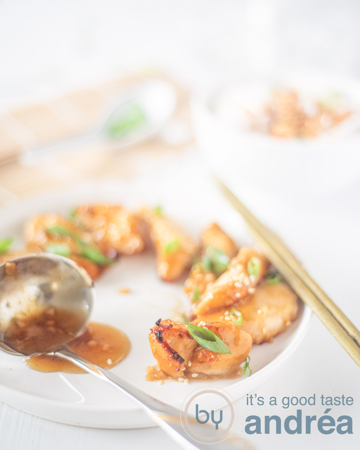 Een wit bord met knapperige kip met sesam Met een sticky honing ketjap saus. Twee chopsticks en wat ingredienten vervangen in de achtergrond