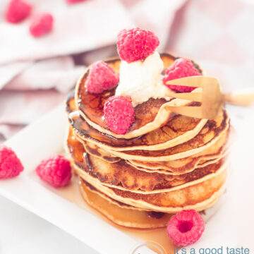 Pancakes met frambozen en crème fraîche op een wit bord. Er omheen meer frambozen. In de achtergrond een wit roze theedoek.