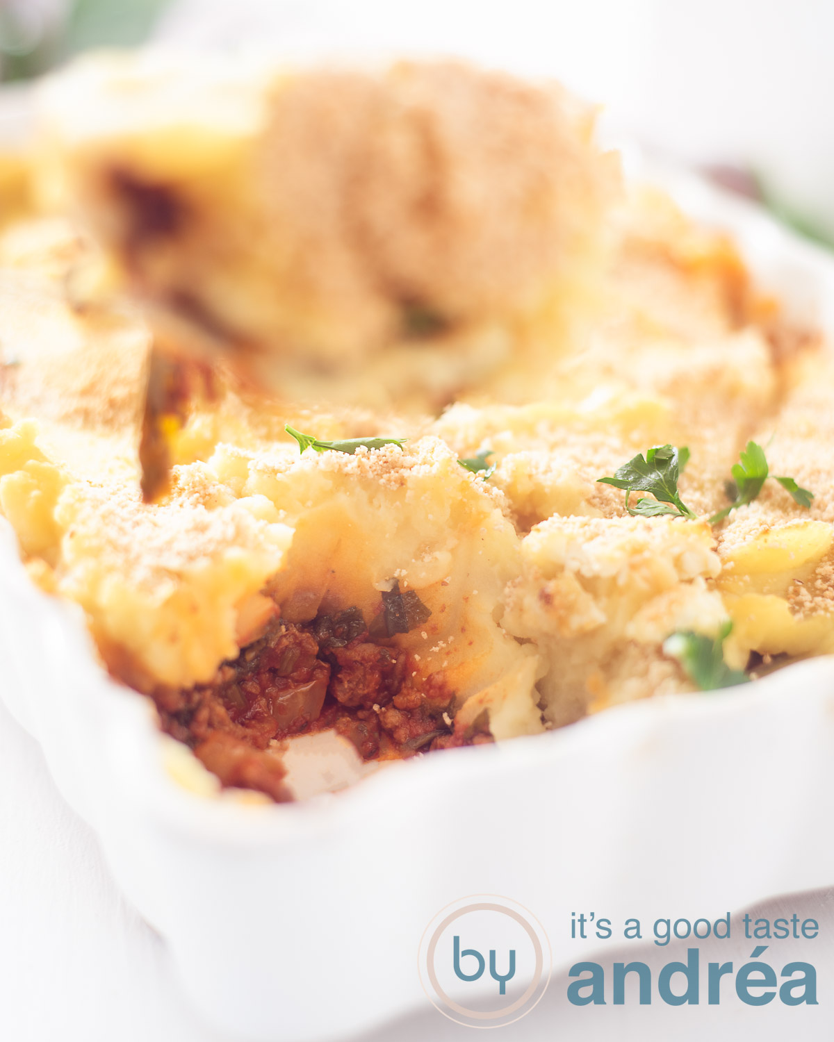 A white oven dish filled with spinach, chopped and topped with mashed potatoes with a crispy crust. A spoon has been scooped out.