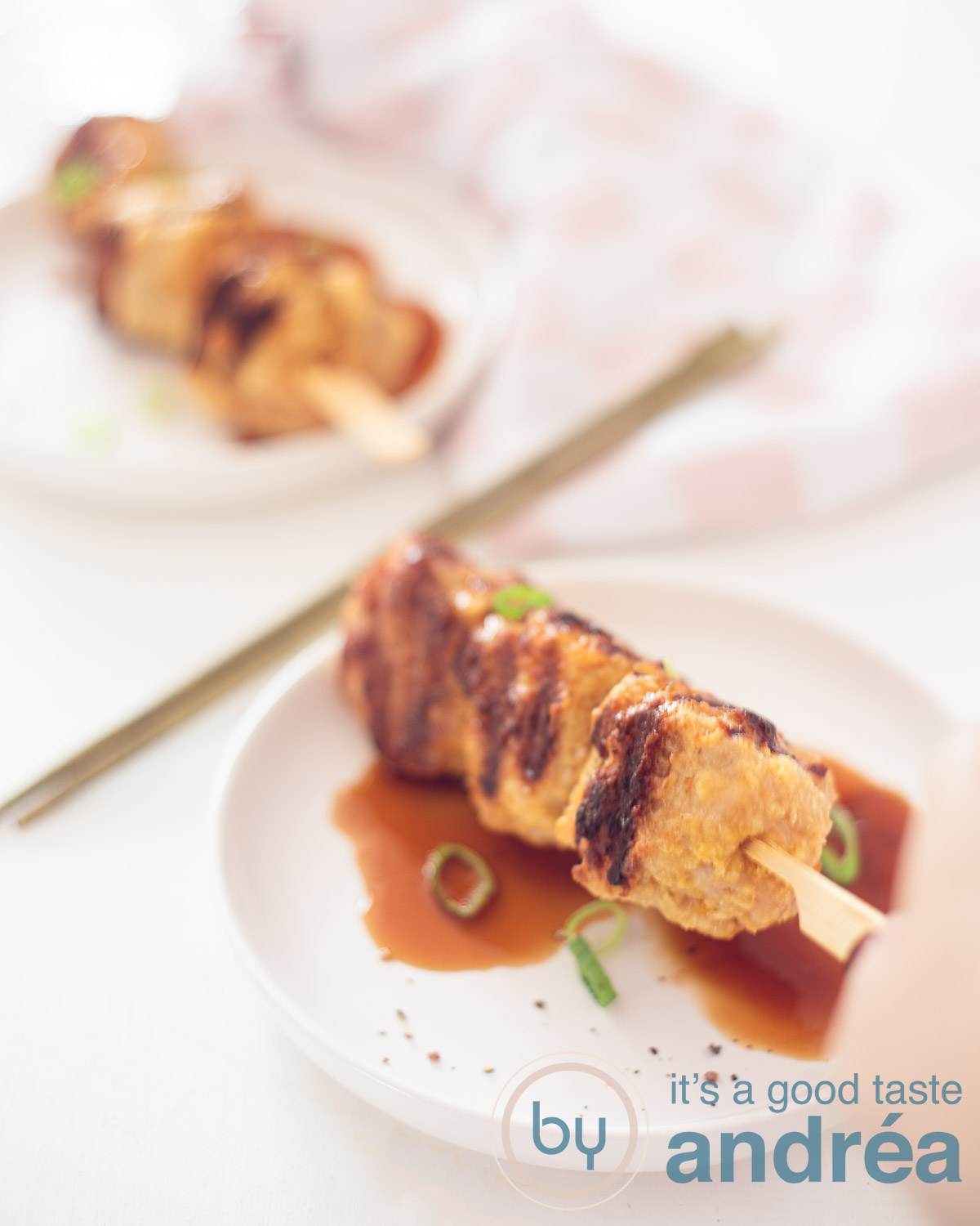 yakitori chicken kebabs on a white plate behind eachother on a white background. With sauce. Two golden chopsticks in between.