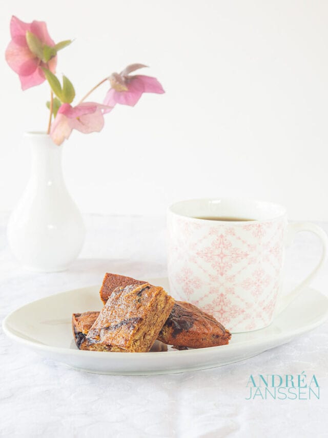 A plate with honey blondies and a pink white cup. In the background a white vase with flowers
