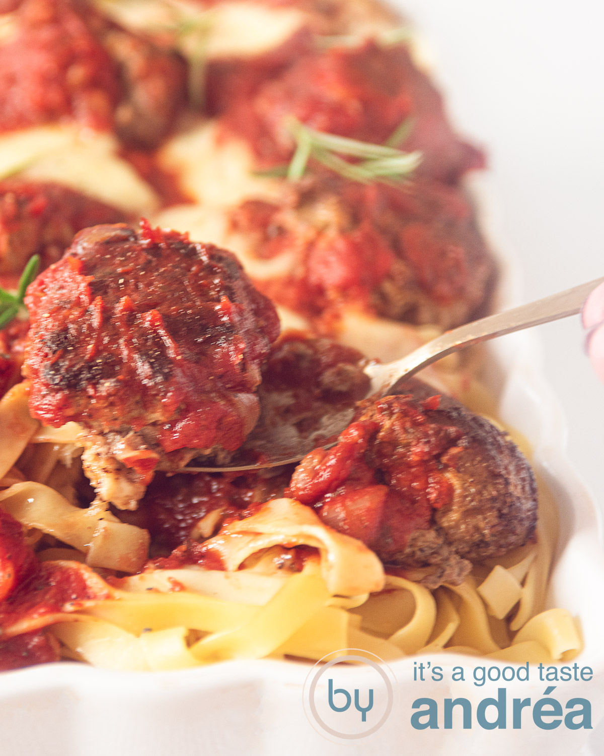 Meatball casserole with tagliatelle in a white casserole dish. A golden spoon taking a meatball.