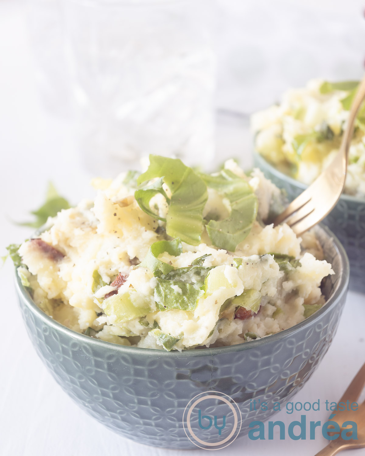 A green bowl filled with raw endive stew with bacon, garlic, butter and cream cheese. A fork pierces it. Two glasses in the background.