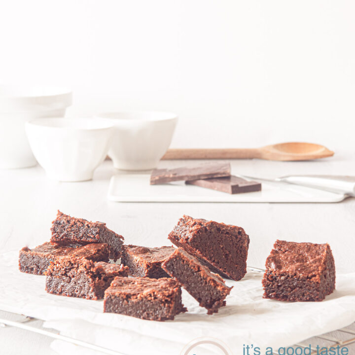 Op een wit bakpapier liggen browneis verspreid. Op de achtergrond een wit kommetje, stukjes chocola en een houten lepel