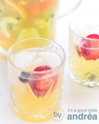 Gember mocktail met komkommer en fruit. Twee glazen op een witte ondergrond en een kan erachter.