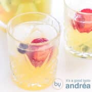 Een vierkante foto met een glas gevuld met een sprite mocktail met fruit. Een tweede glas deels er schuin achter.