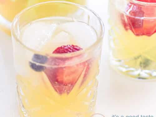 Een vierkante foto met een glas gevuld met een sprite mocktail met fruit. Een tweede glas deels er schuin achter.