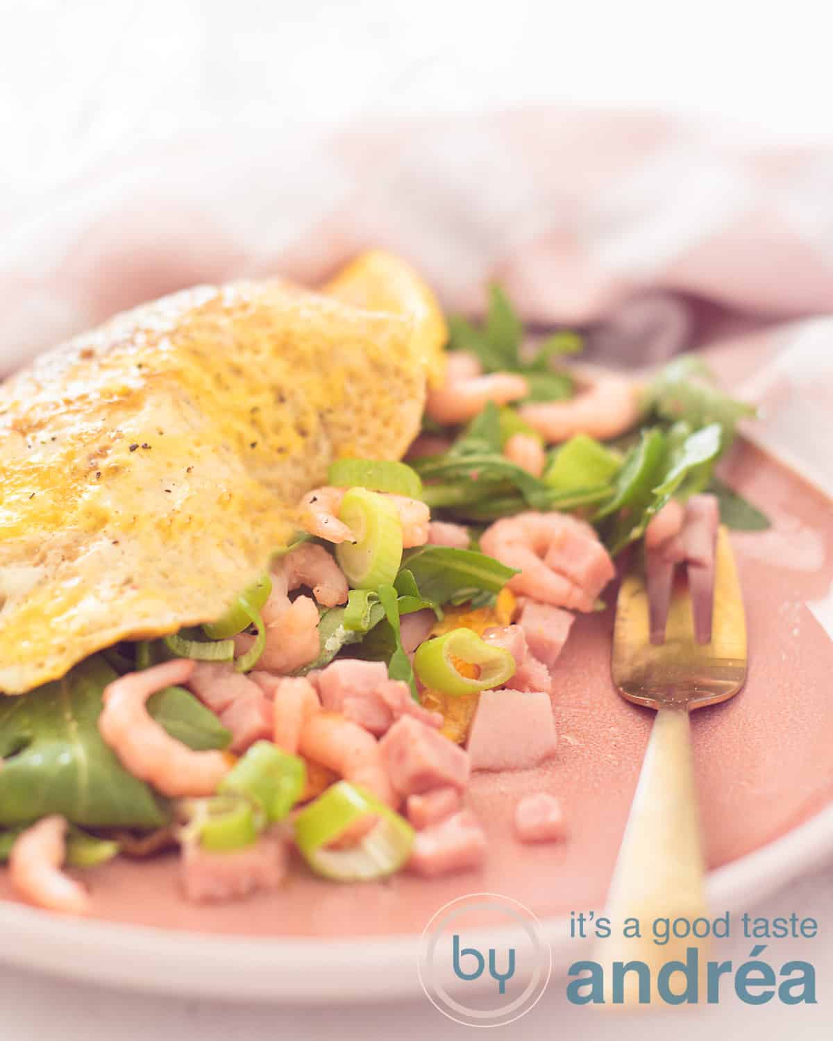 Een roze bord met een omelet gevuld met garnalen, hamblokjes, rucola en lenteui. Een gouden vork ligt er naast.