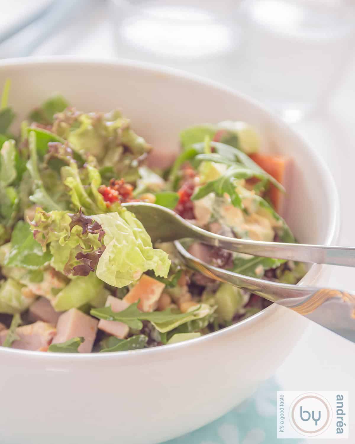 Part of a bowl of green salad with pesto, chicken and tomatoes