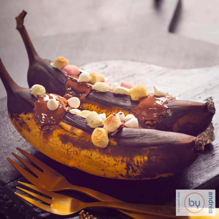 Een vierkante foto met twee gegrilde bananen achter elkaar op smaak gebracht met whisky, gesmolten chocola en marshmallows