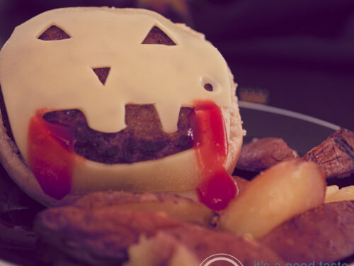 Een vierkante foto met een zwart bord met zelfgemaakte frietjes en een Halloween hamburger met kaas.