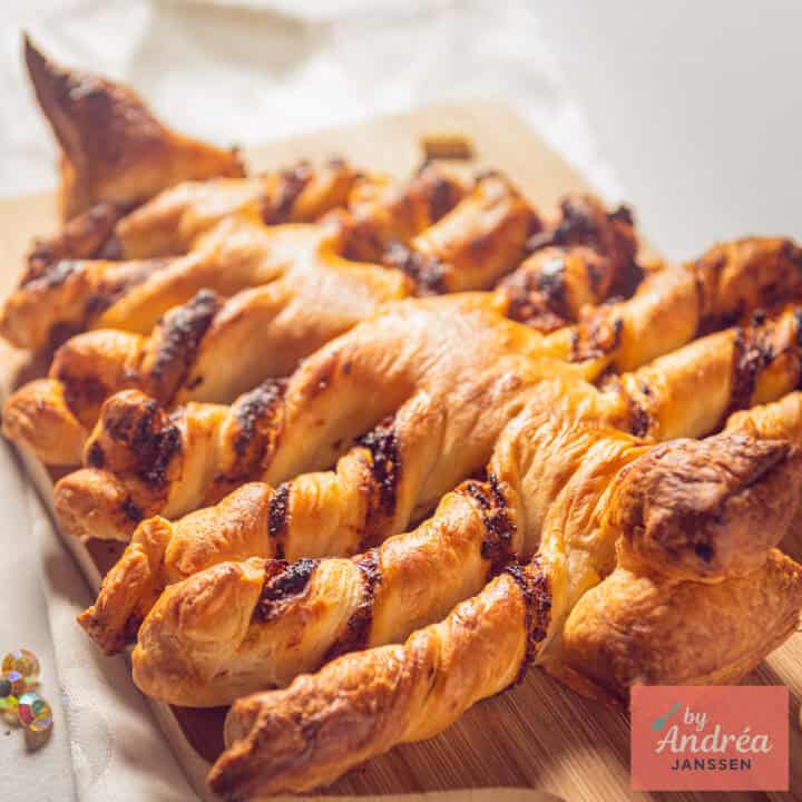 Een vierkante foto met een kerstboom van bladerdeeg en rode pesto op een stuk bakpapier.