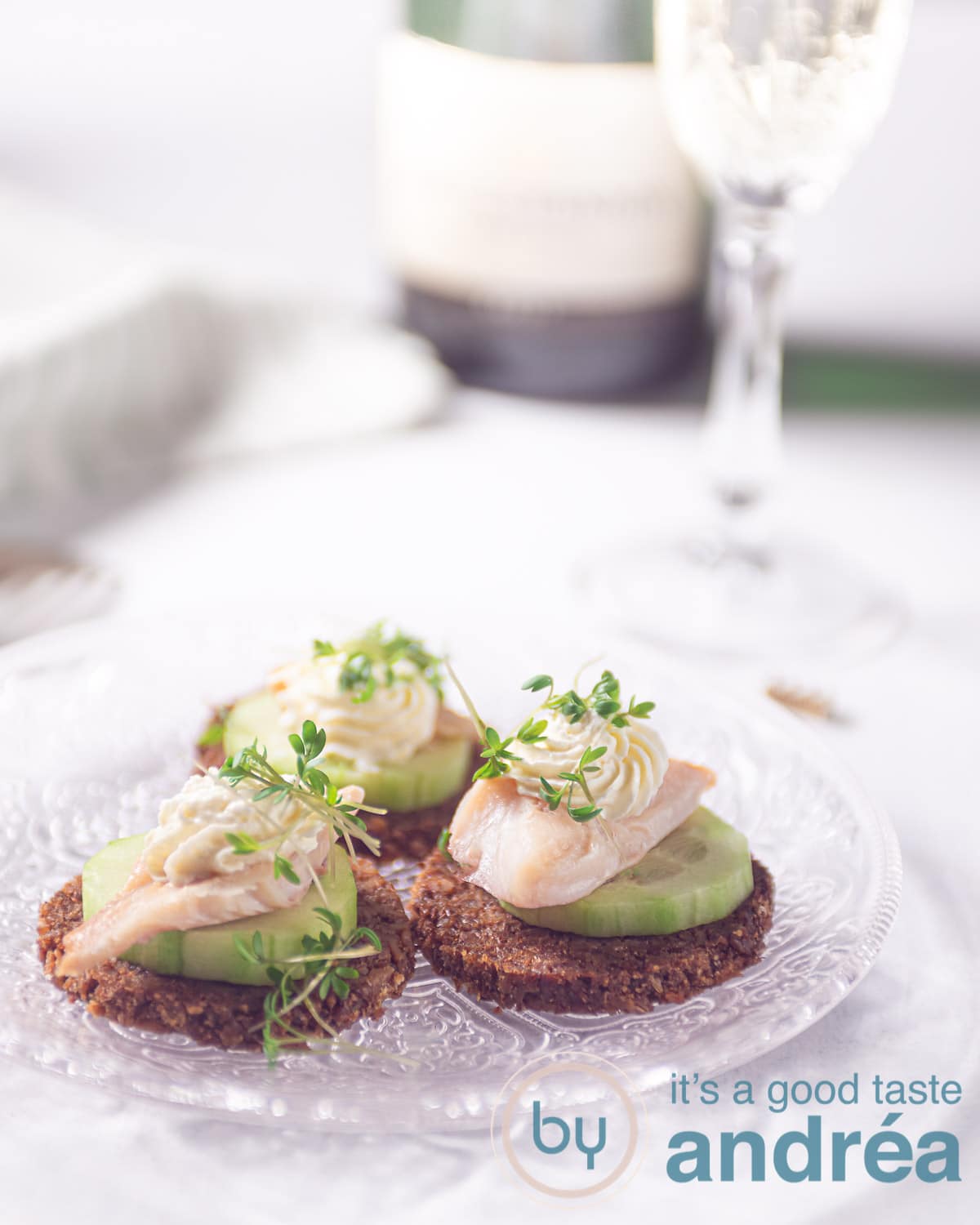 three smoked trout snacks with cucumber and rye bread on a glass plate
